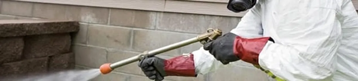 Pest control technician applying exterior insect treatment along a home foundation in Sarasota, FL