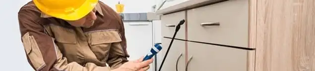 Roach exterminator applying treatment under kitchen cabinets in Sarasota, FL
