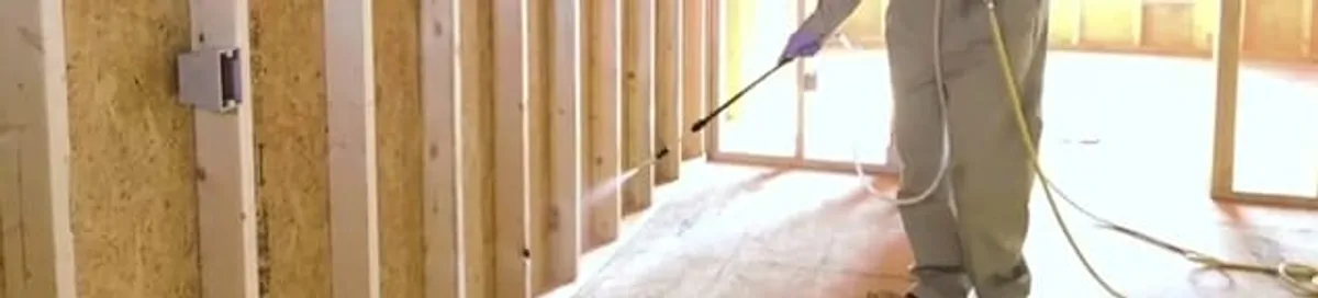 Termite treatment technician applying spray along framing and unfinished walls in Sarasota, FL
