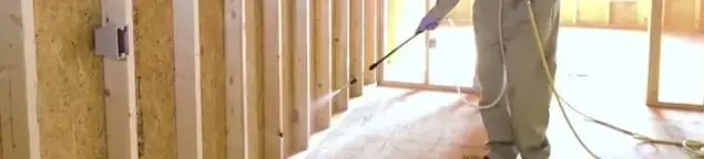 Termite treatment technician applying spray along framing and unfinished walls in Sarasota, FL